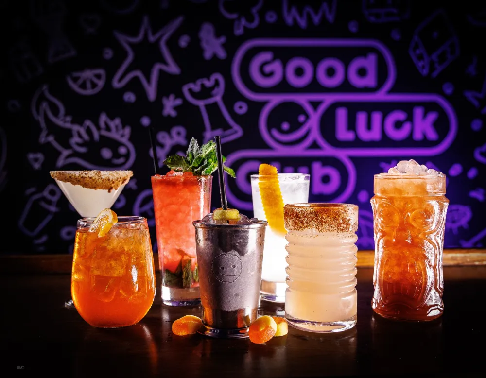 Every cocktail on the menu lined up in front of the glowing mural