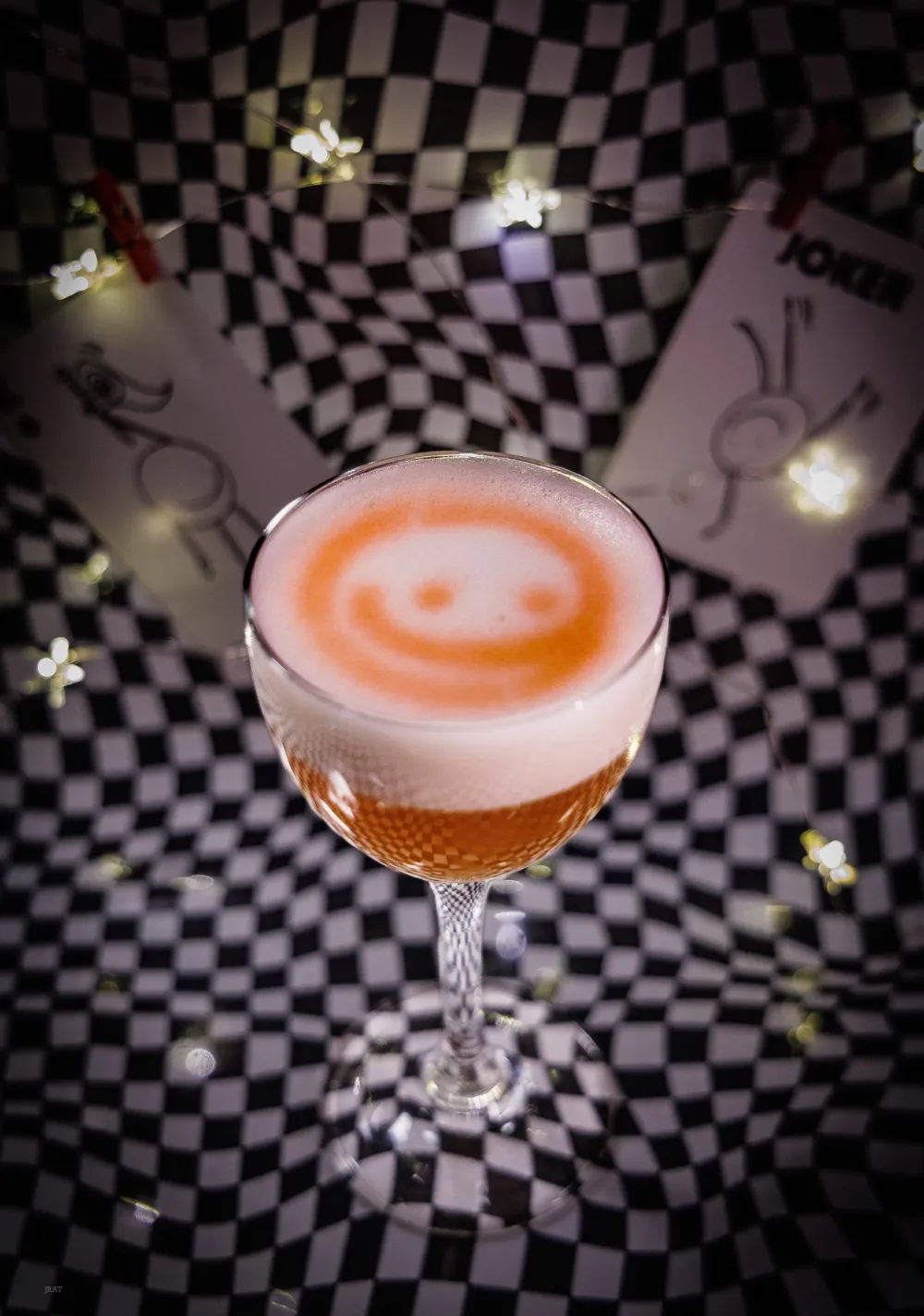 Amaretto Sour with a smiley face drawn in the foam, on a checkerboard backdrop