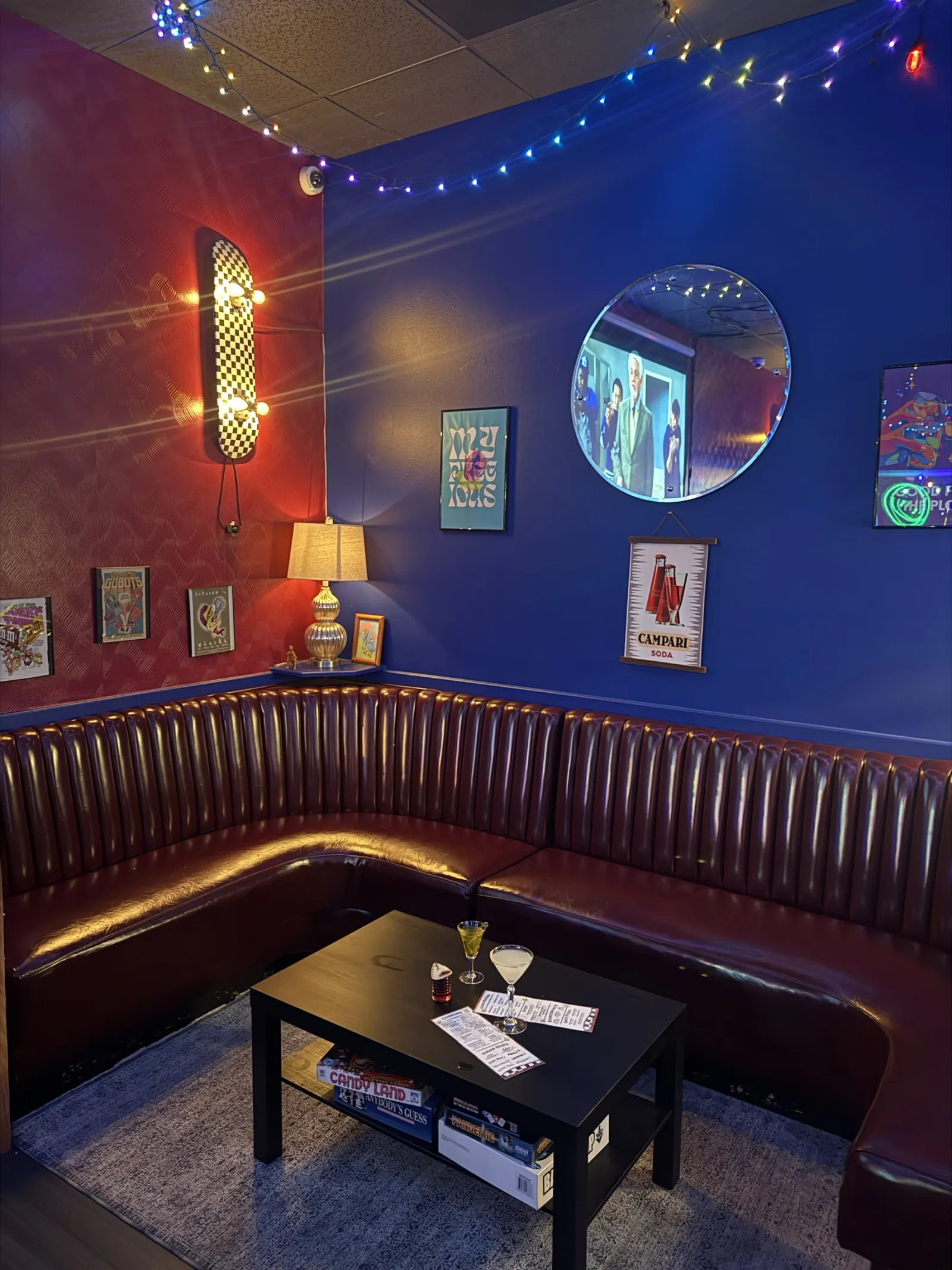 A maroon leather booth corner with a coffee table, a round mirror and framed art