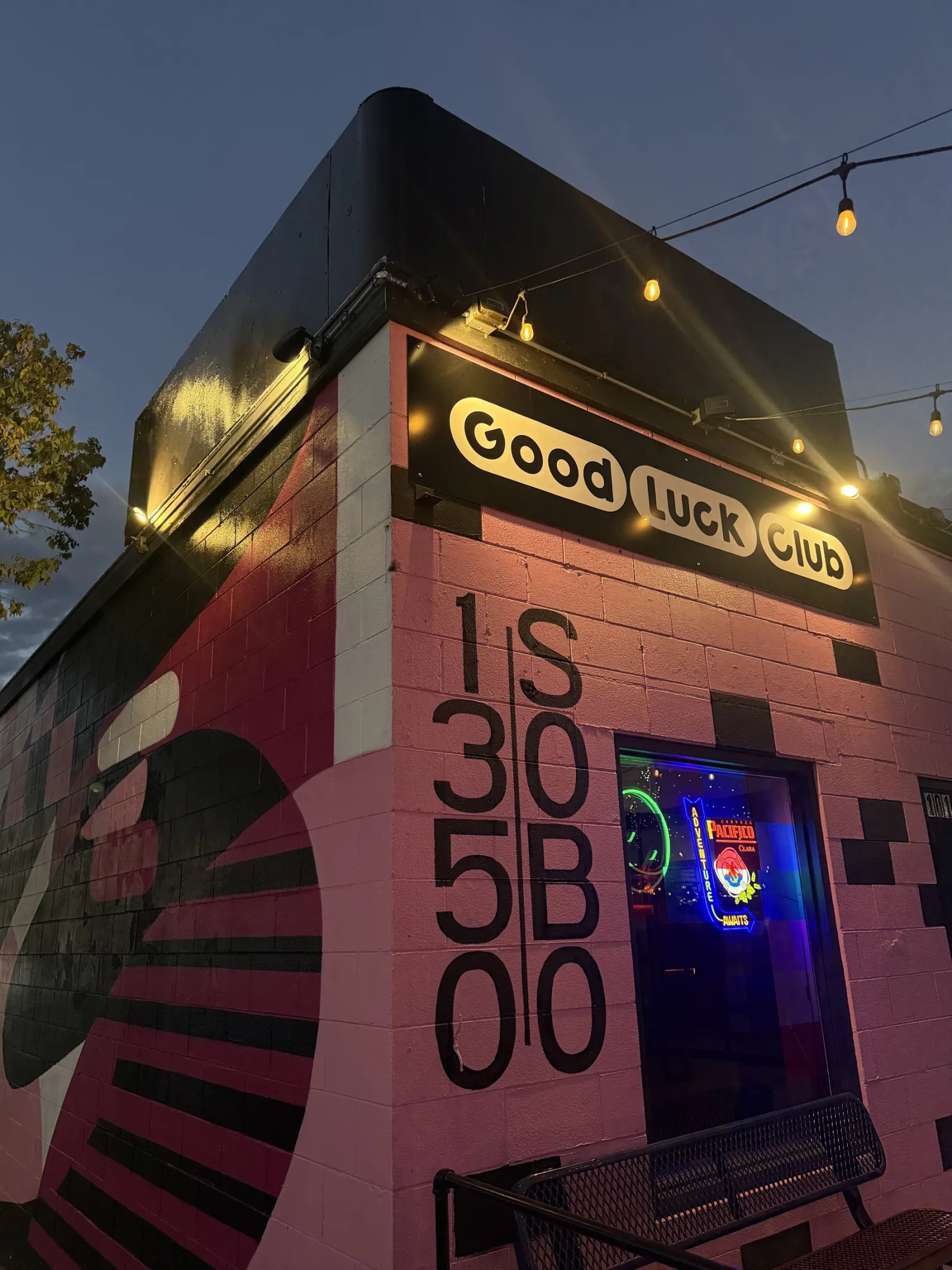 The pink Good Luck Club building at dusk, capsule sign on the roof and 1350 S Bro painted down the side