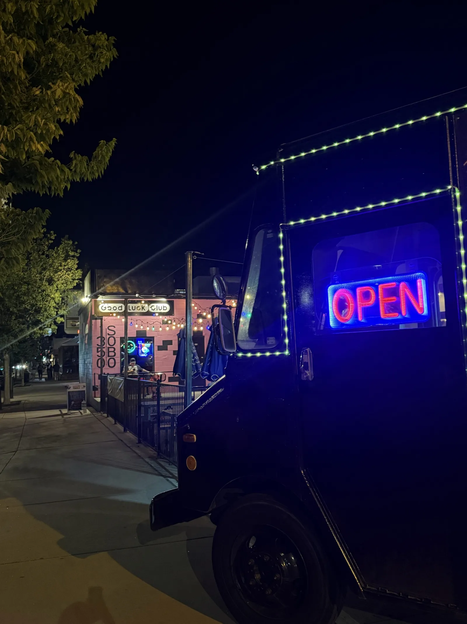 A food truck with a lit OPEN sign parked out front at night