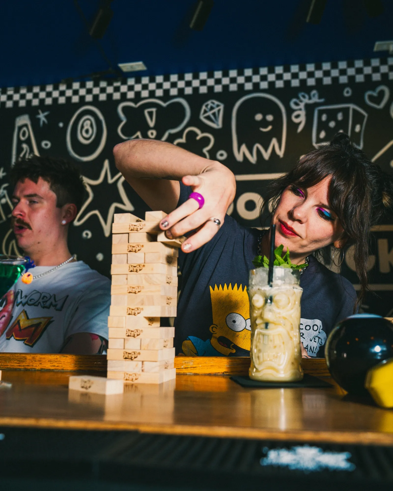 Two guests playing Jenga at the bar, a tiki drink beside the tower