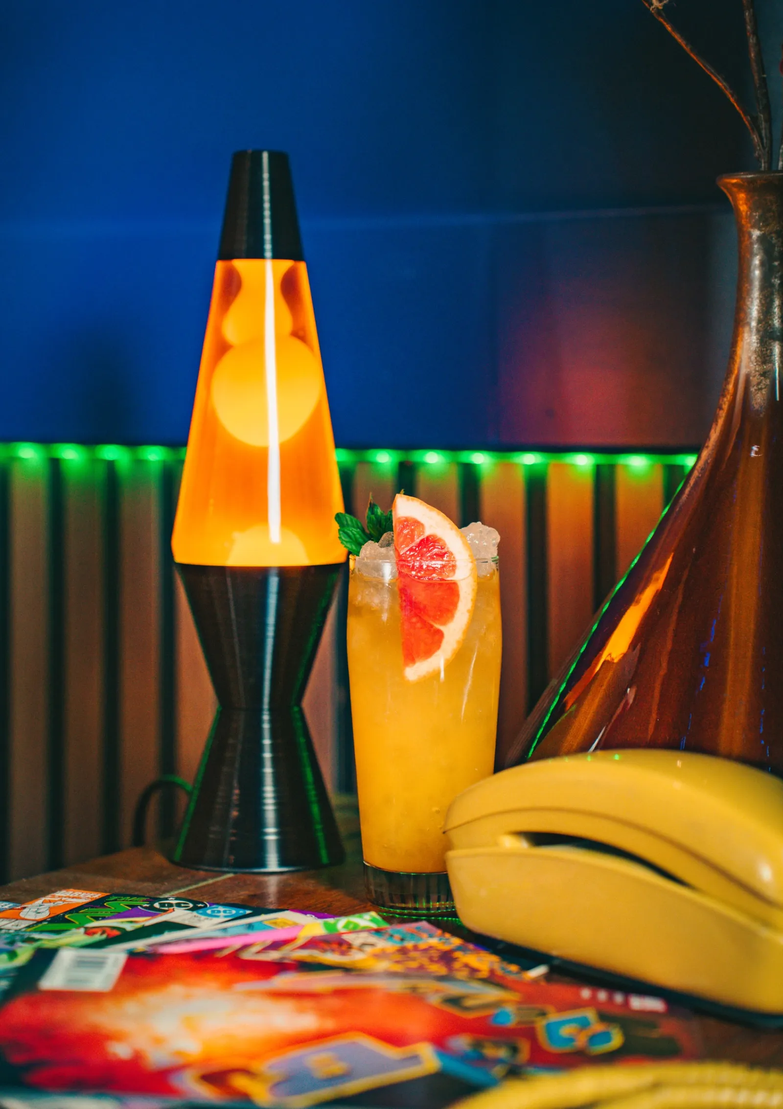 A grapefruit cocktail next to a lava lamp and a yellow rotary phone