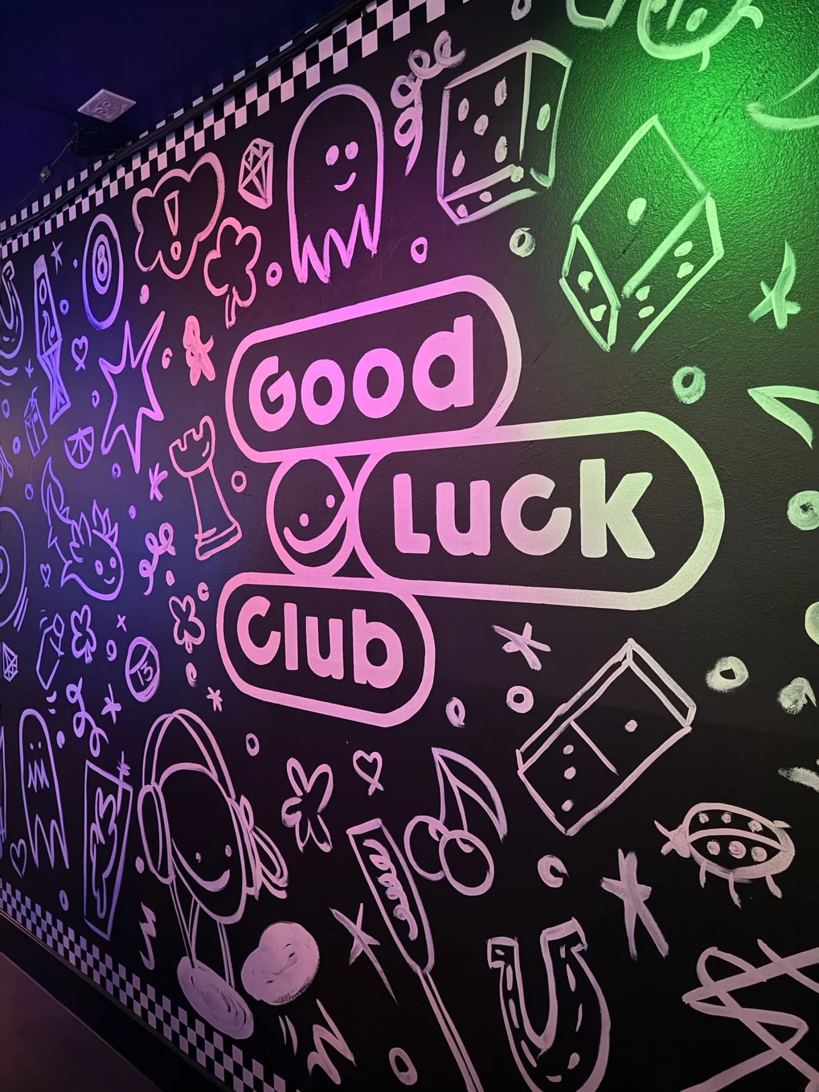 The doodle mural with the Good Luck Club logo, lit pink and green