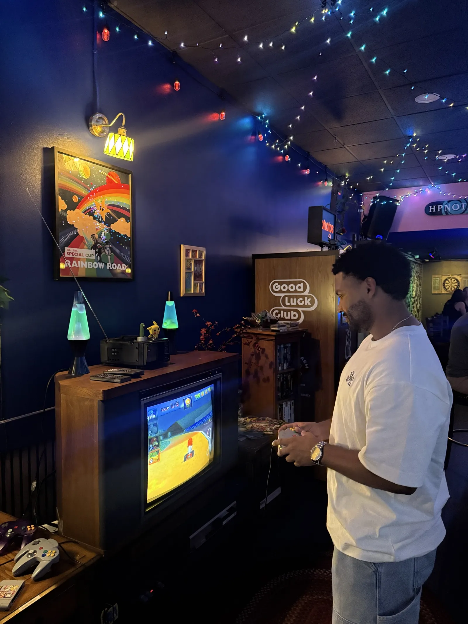 A guest playing N64 on an old TV in the game corner, a lava lamp on the shelf