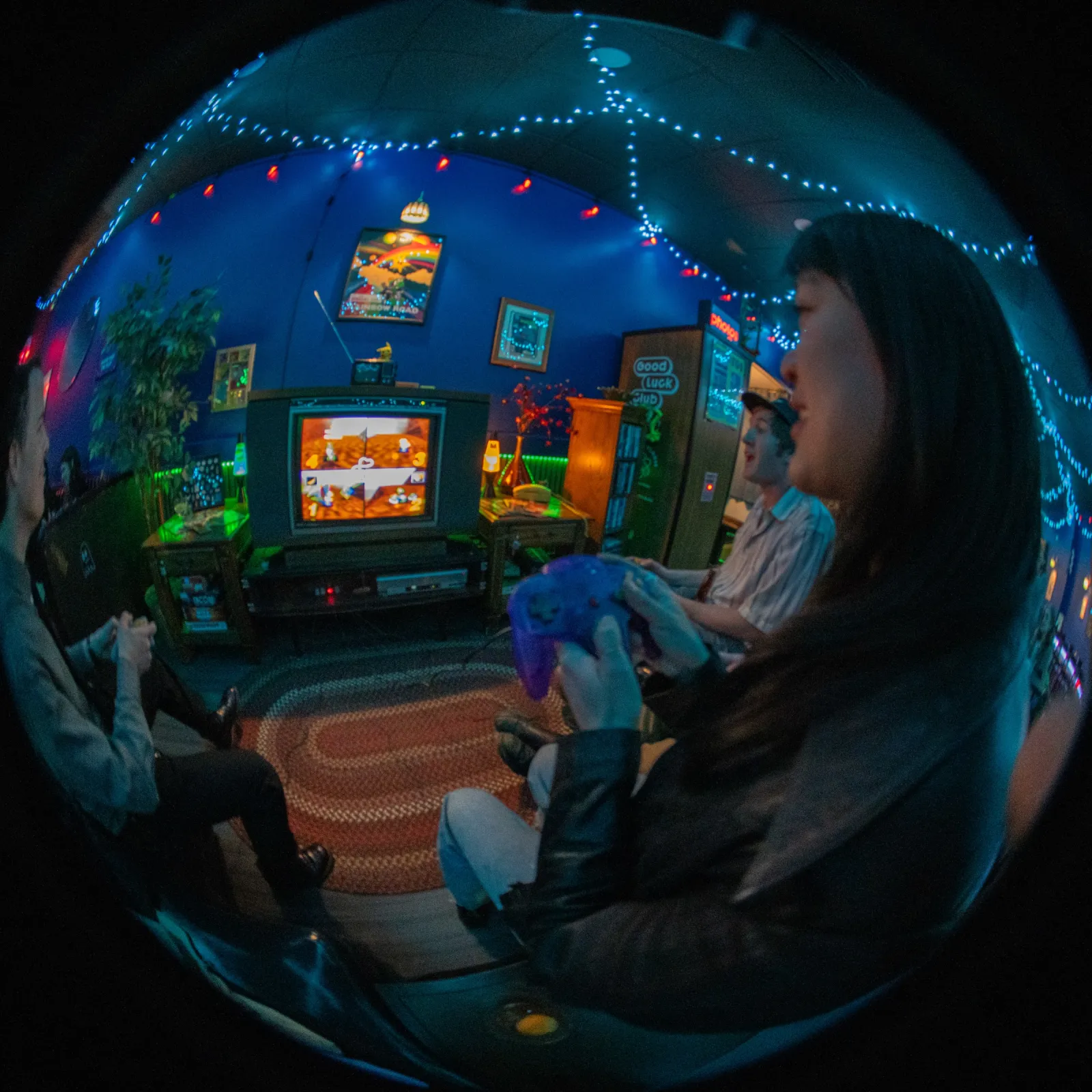 Fisheye shot of friends playing N64 on an old TV under the string lights