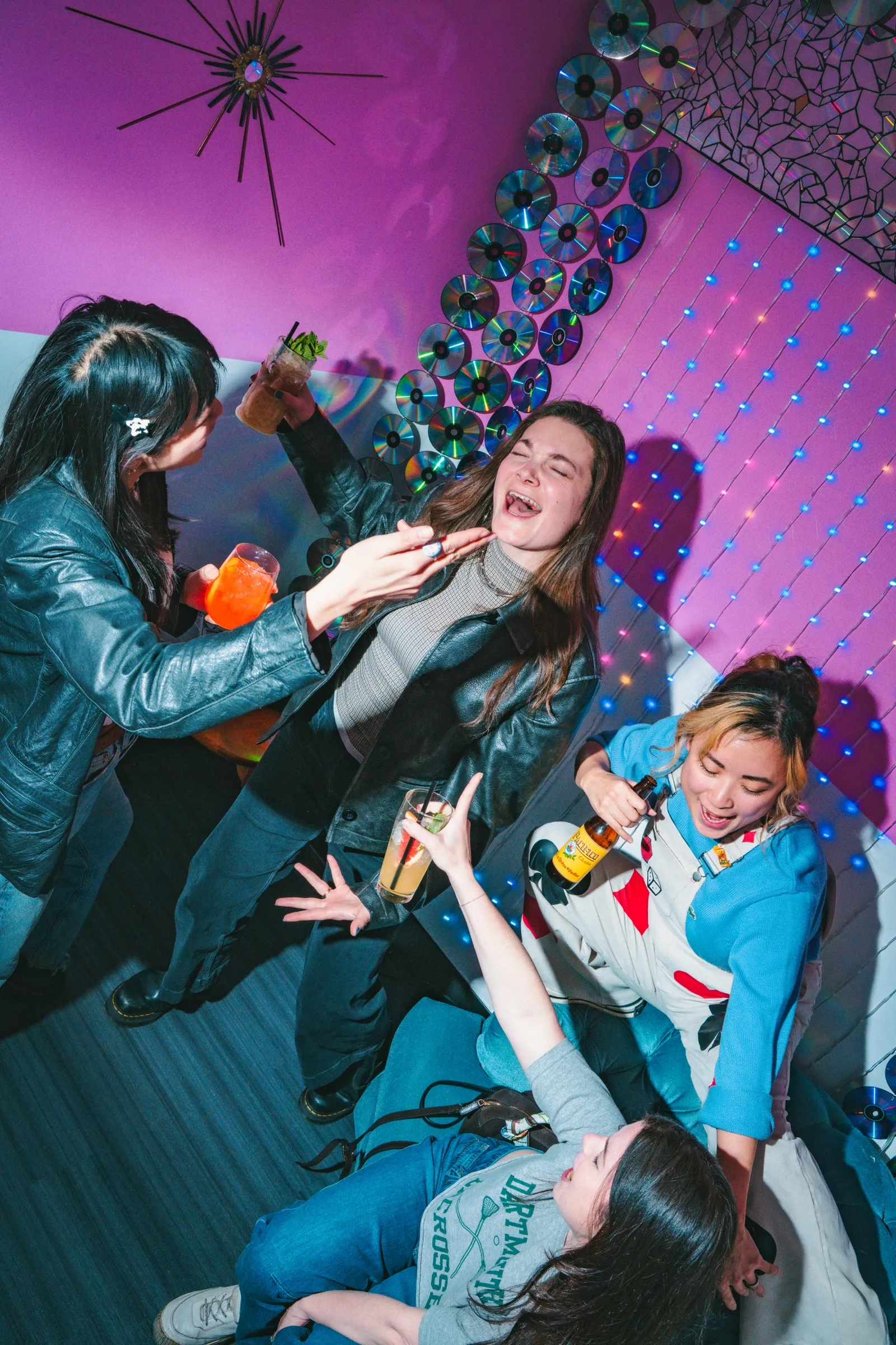 Friends piling onto a velvet couch in the pink room, a wall of CDs behind them